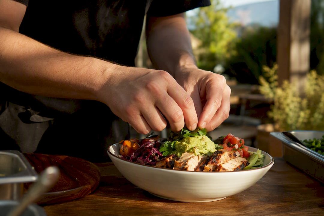 Hands assembling paleo Mexican bowl in kitchen