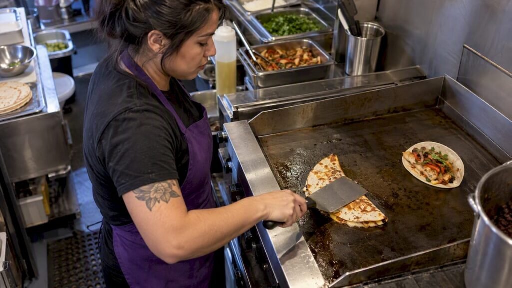Cook pressing quesadilla beside soft taco