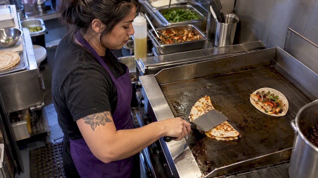Cook pressing quesadilla beside soft taco